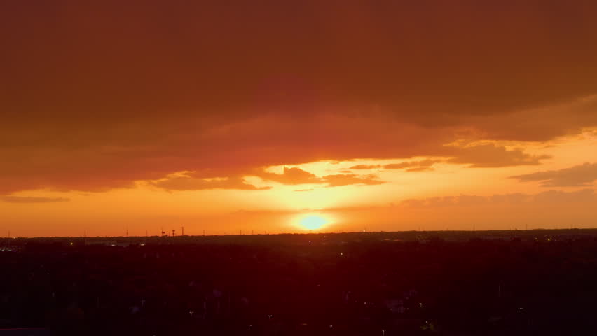 Orange sunset with clouds glowing above distant landscape during golden hour evening sky at dusk
