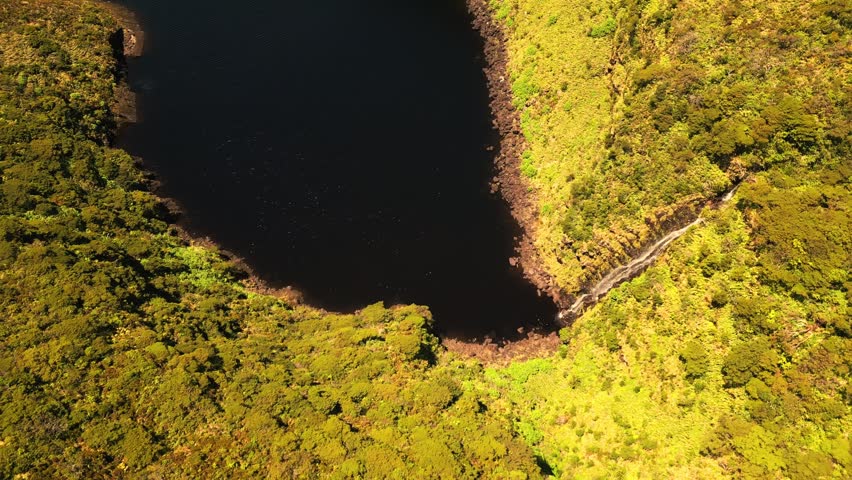 Aerial view of lush green hills surrounding a dark lake with a visible hiking trail