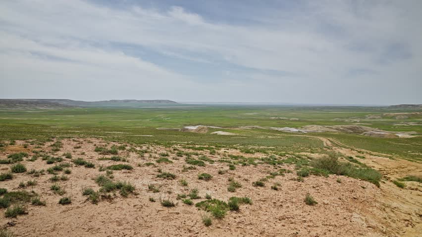 Wide-angle view of a vast landscape featuring rolling hills and grassy plains under a clear sky, highlighting natural beauty and tranquility