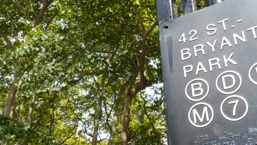 New York City subway entrance sign on 42 street near Bryant Park, United States. American underground transportation, Manhattan Midtown transport. Metropolitan station near public Library, green trees