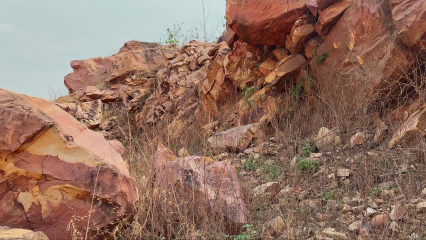 Slow push in shot toward a rugged rocky outcrop featuring fractured boulders weathered stone surfaces and dry grass vegetation Natural textures and mineral rich formations dominate the landscape