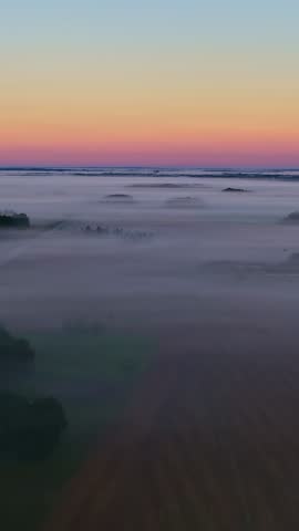 A foggy rural landscape at dawn with colorful horizon, wide shot.