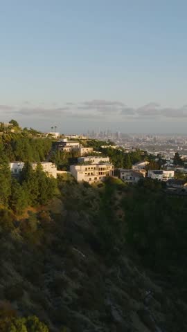 Backwards reveal of luxury residences in hills above metropolis. Hollywood Hills at golden hour. Los Angeles, California, USA