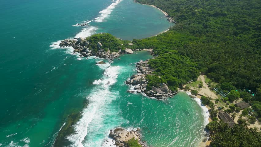 Aerial high altitude pullback above dramatic Cabo San Juan twin beaches with turquoise water rocky headlands and jungle coastline at Parque Tayrona Colombia