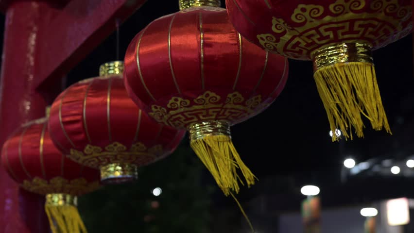 Traditional Red Asian Lanterns with Golden Patterns at Decorative Street Entrance. Red decorative Asian lanterns made of shiny satin-like fabric with golden patterns and tassels hanging at a traditional street entrance. Cultural architectural details and festive atmosphere in an outdoor urban setting.