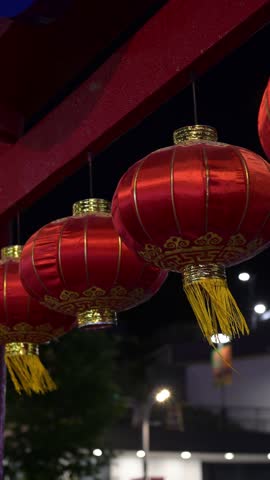 Traditional Red Asian Lanterns with Golden Patterns at Decorative Street Entrance. Red decorative Asian lanterns made of shiny satin-like fabric with golden patterns and tassels hanging at a traditional street entrance. Cultural architectural details and festive atmosphere in an outdoor urban setting.