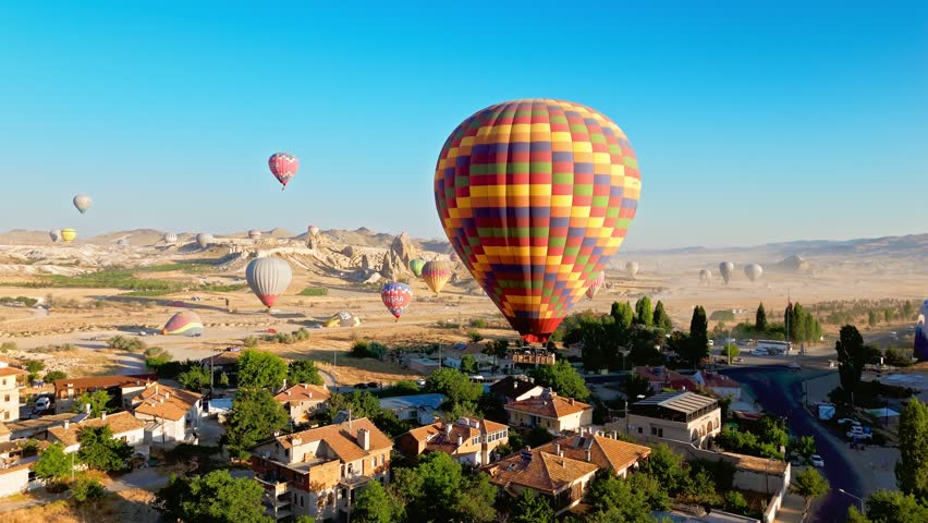 Drone view of Cappadocia, Turkey. Hot air balloon flight over village houses, rocky valleys and bright morning sky.