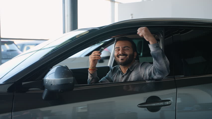 Happy Indian man showing new car keys in dealership showroom