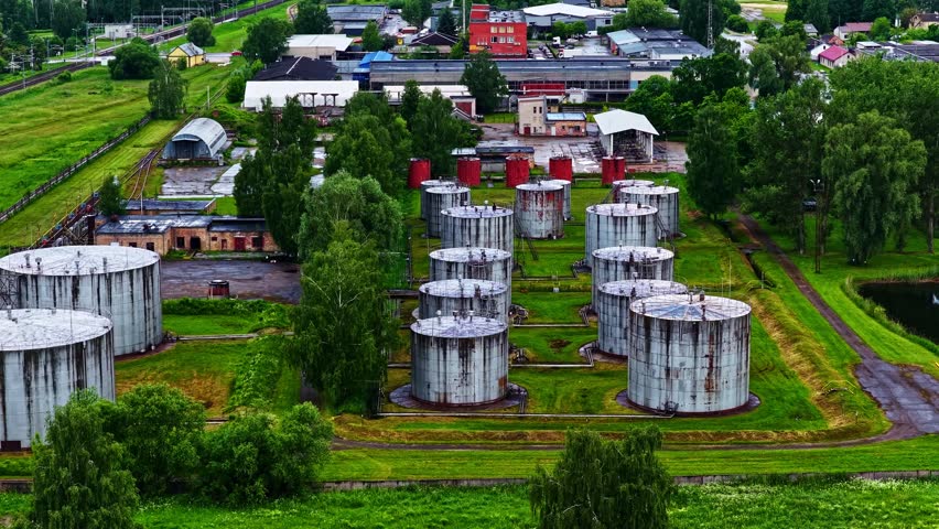 Industrial oil storage tanks at a refinery complex surrounded by green trees and railroad