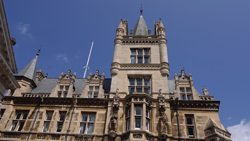 Low angle view of Gonville and Caius College, a historic building of the University of Cambridge, showcasing its intricate architecture and towering presence against a clear blue sky