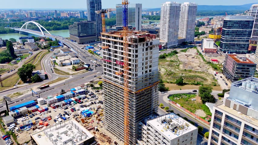 Bratislava, Slovakia, 2 June 2026: Modern urban development, Bratislava, Slovakia. Vertical drone shot of a concrete skyscraper under construction next to streets and a parking lot.