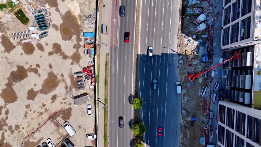 Drone view of urban highway traffic, Bratislava, Slovakia. Top down perspective of cars driving on multi lane road next to building shadow and construction area.