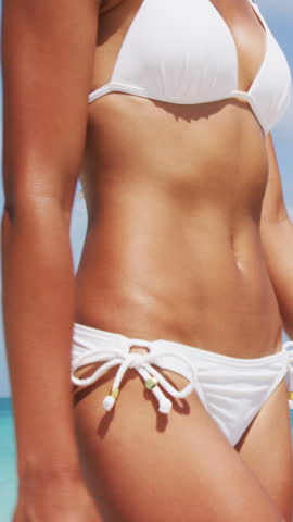 Healthy slim woman with flat stomach closeup. Vacation Travel Beach Life. Woman in bikini walking on paradise beach with white sand turquoise water. Video is unretouched and model without makeup.
