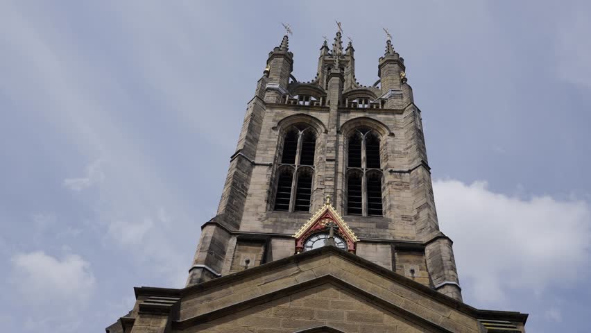 Low angle view of St. Nicholas Cathedral s central tower with its clock and pointed roof, standing tall against a cloudy sky in Newcastle upon Tyne