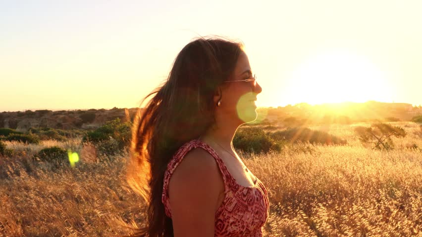 A beautiful young woman with outstretched arms enjoys the serene golden hour in a sun-drenched field. Her joyful expression captures the essence of freedom, happiness, and peace in nature