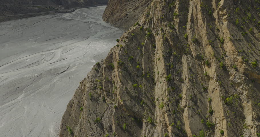 Drone gliding shot moving past steep textured rocky cliffs revealing the wide braided riverbed of the Kali Gandaki valley in Mustang, Nepal
