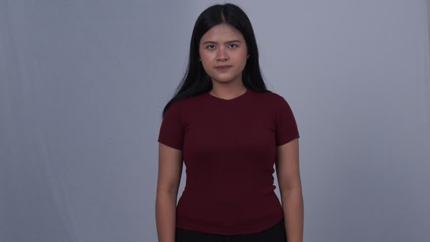 Sweet young Asian woman in maroon dress smiling and putting black bag on her shoulder and pointing forward seen from front side