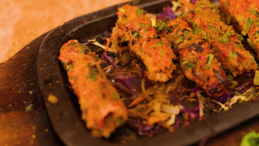 Fork picks up grilled meat kebabs from a steaming sizzler plate with vegetables.