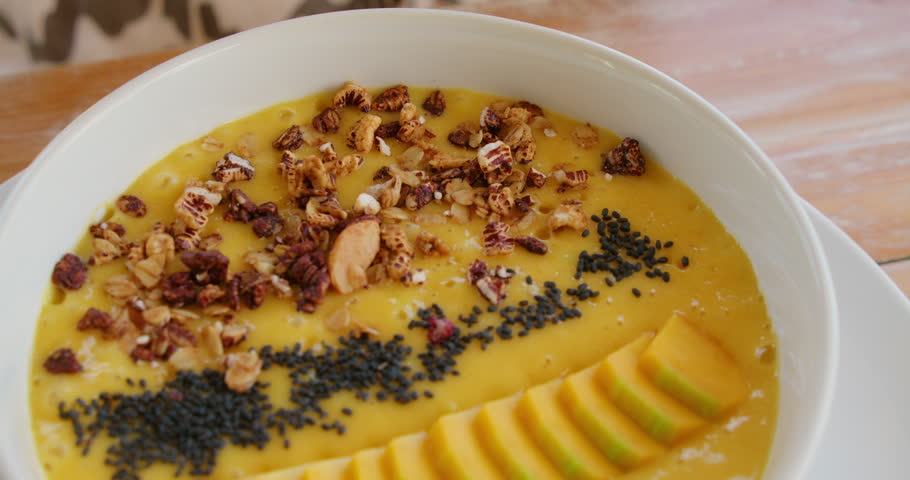 Yellow mango smoothie bowl decorated with fruit slices granola and black seeds