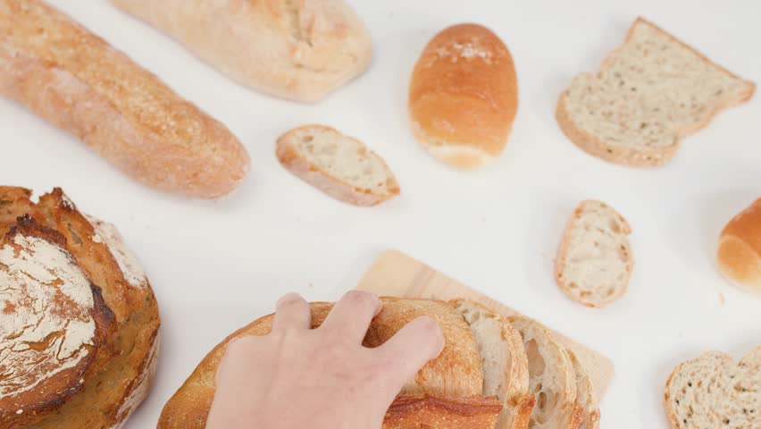 Top-down view of hands slicing crusty sourdough loaf on wooden board with bright lighting.
