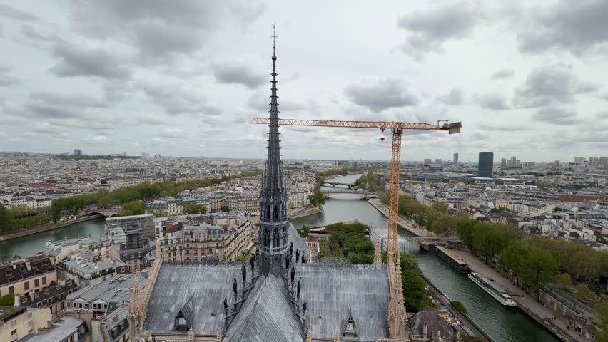 Aerial view tracking down the famous spire of Notre Dame Cathedral, revealing the intricate gothic architecture and the surrounding Paris cityscape with the River Seine flowing below