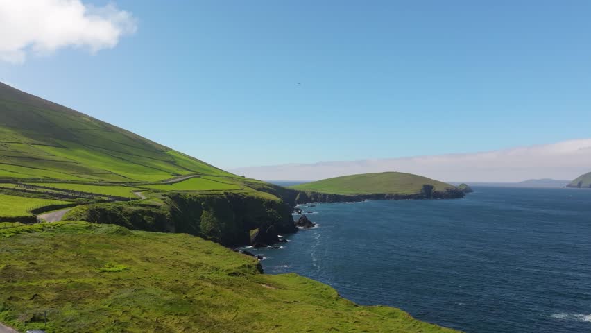 Lush green hills slope gently towards the ocean along Ireland
