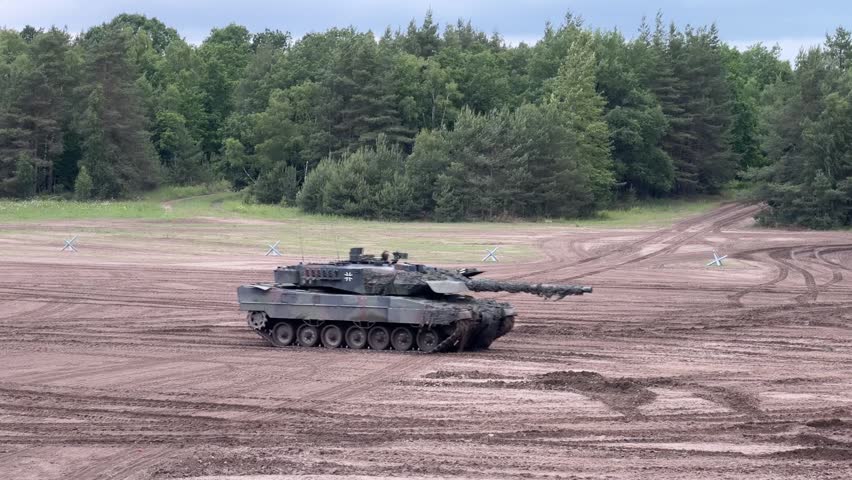 German Leopard 2 tank moves slowly across muddy training ground with forest backdrop
