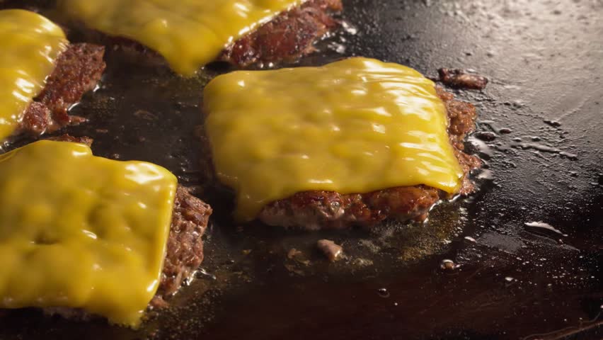 Spatula Lifting juicy smash burger patties topped with melted American cheese sizzling on a hot flat top griddle