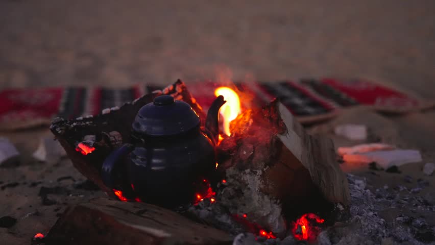 Close Up Campfire Embers with Traditional Bedouin Rug and Tea Kettle in Desert Egypt at night
