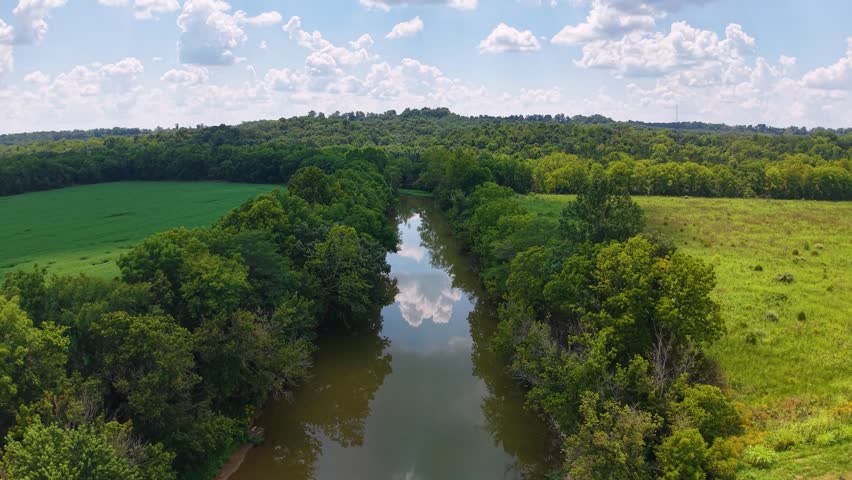 Aerial drone view of a winding river flowing through lush forest and farmland near Serpent Mound in Ohio