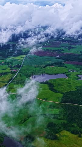 Aerial view of green farmland and lakes with low clouds drifting over rural landscape