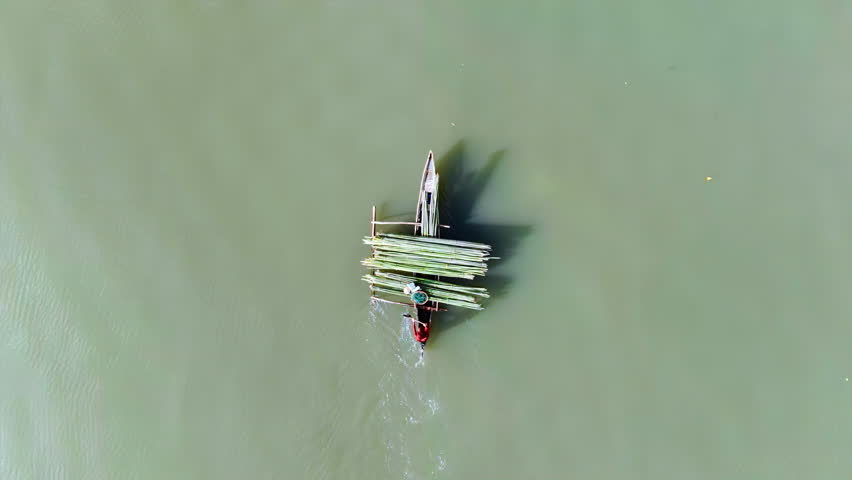 Bird eye view tracking drone shot of a fisherman paddling an outrigger boat carrying loads of bamboo sticks in the brackish waters of Malampaya Inner Sound.