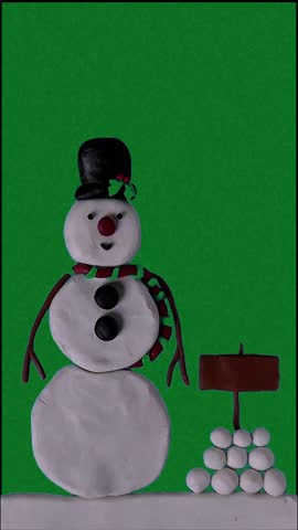 A clay snowman wearing a black top hat and red scarf on a green background with a yellow moon and pile of small white snowballs