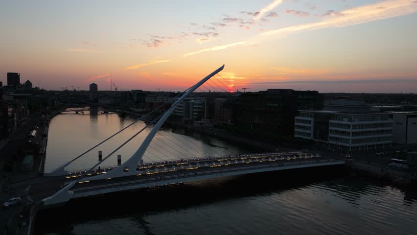 The Samuel Beckett Bridge stands against a vibrant sunset, with reflections on the River Liffey. Ideal for cityscape and architectural themes.
