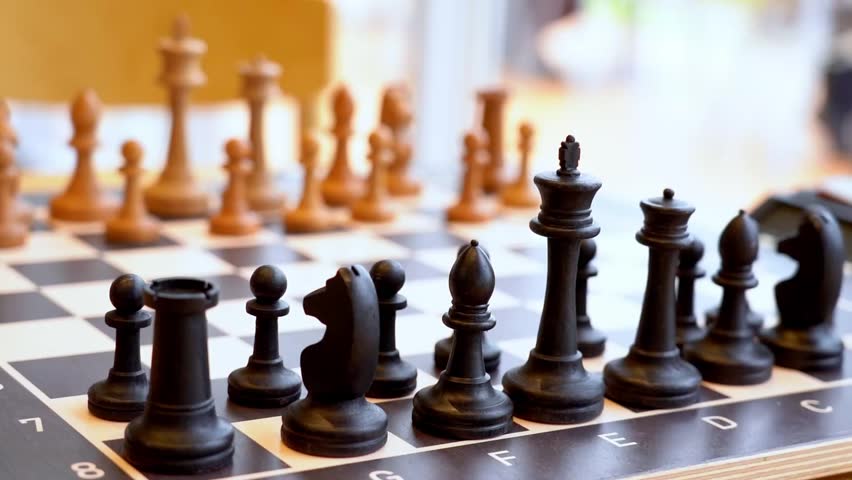 Close-up of black and white chess pieces on a wooden board. Shallow depth of field highlights game setup details. Ideal for educational content and game strategy demonstrations
