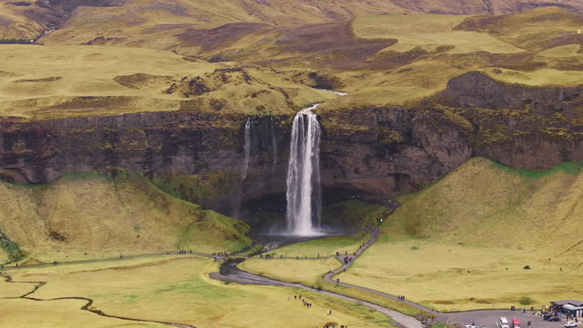 Seljalandsfoss waterfall in Iceland, visitors on walkway walking towards cave.