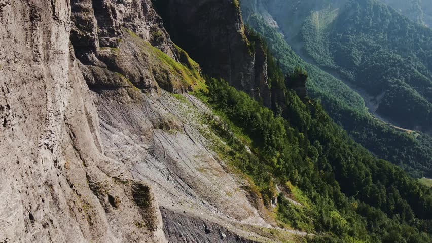 Aerial view of the rugged rock faces and steep slopes of the French Alps, with dense green forests and mountain terrain in Chamonix, Auvergne-Rhone-Alpes, France.