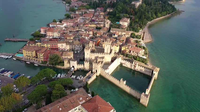 Stunning aerial view of the medieval Scaligero Castle and its fortified harbor in Sirmione, Italy. Features the historic stone fortress alongside the scenic resort town on the shores of Lake Garda.