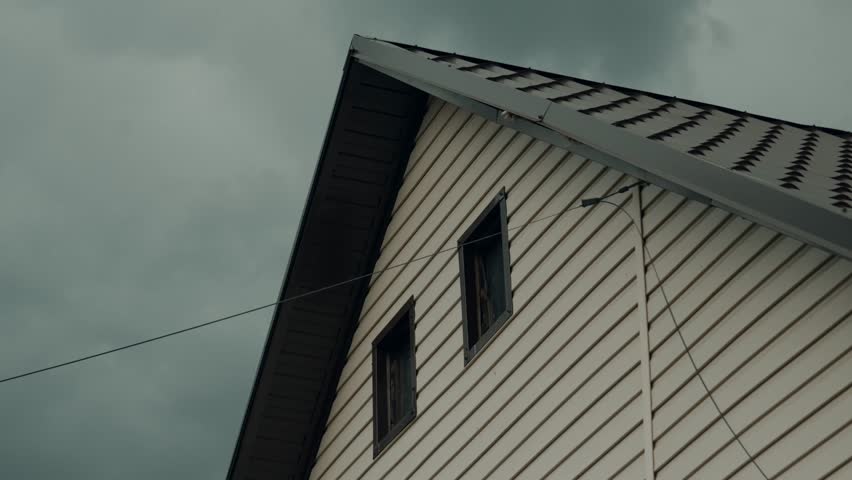A close-up of the upper floor of a rustic house from the outside, with windows and an attic, electrical wiring, trim, and tiles.