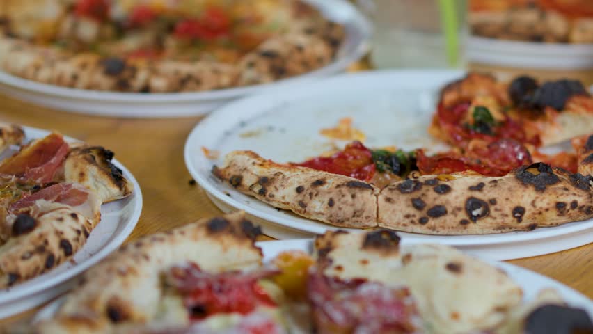 Close-up shot of hands taking slices of fresh pepperoni pizza from a wooden table.