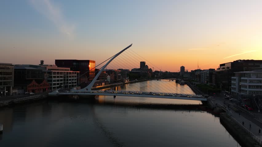 The Samuel Beckett Bridge spans the River Liffey as the sun sets over Dublin. Ideal for travel documentaries and urban landscape features.