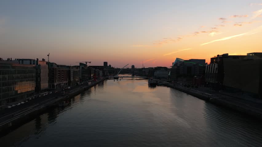 The sun sets over the River Liffey, highlighting the Samuel Beckett Bridge and surrounding architecture. Ideal for use in travel content or cityscape projects.