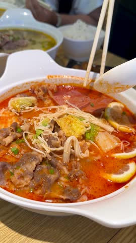 Close-up of person using chopsticks and spoon to eat spicy beef noodle soup.