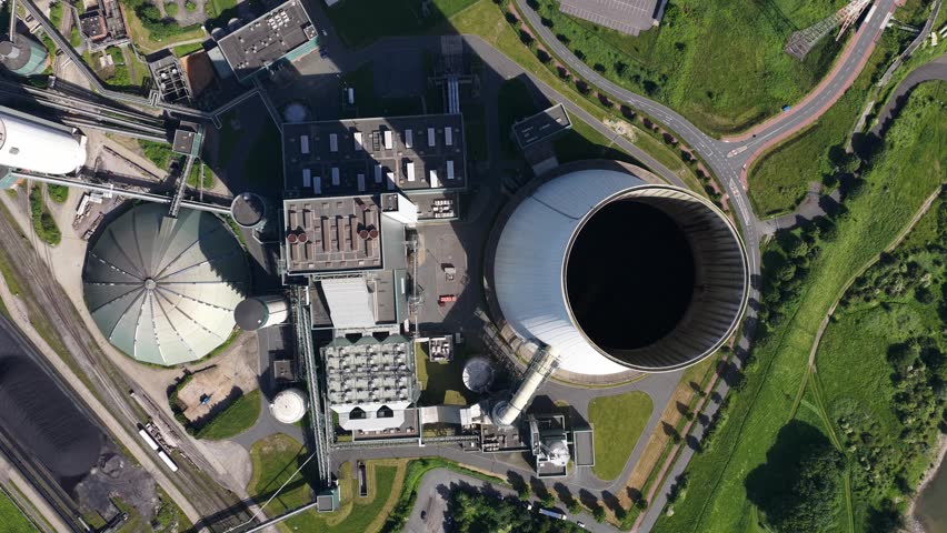 Impressive top down aerial view of a coal fired power plant with a massive cooling tower, showcasing industrial energy production and the surrounding infrastructure on a sunny day