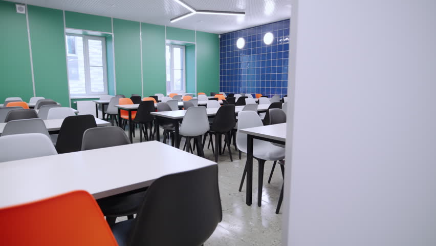 School cafeteria features empty furniture sets under stylish ceiling lamps. Colorful interior design promotes lively lunch hour atmosphere