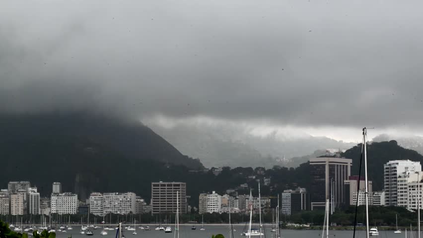 View of the city skyline and harbor with sailboats under a heavy overcast sky and misty mountains in Rio de Janeiro, State of Rio de Janeiro, Brazil.