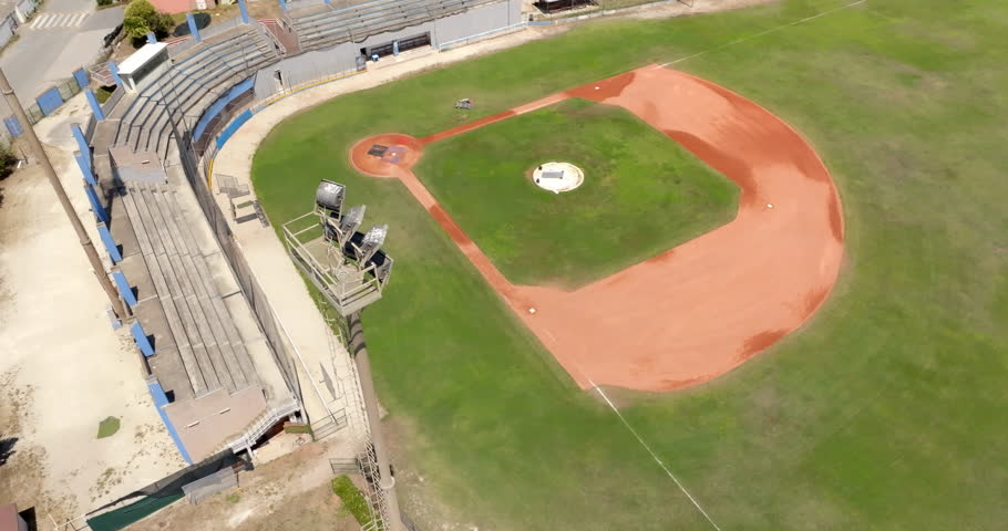 An overhead top down drone view of a baseball diamond, showing its green grass infield, the red clay base paths, a pitcher