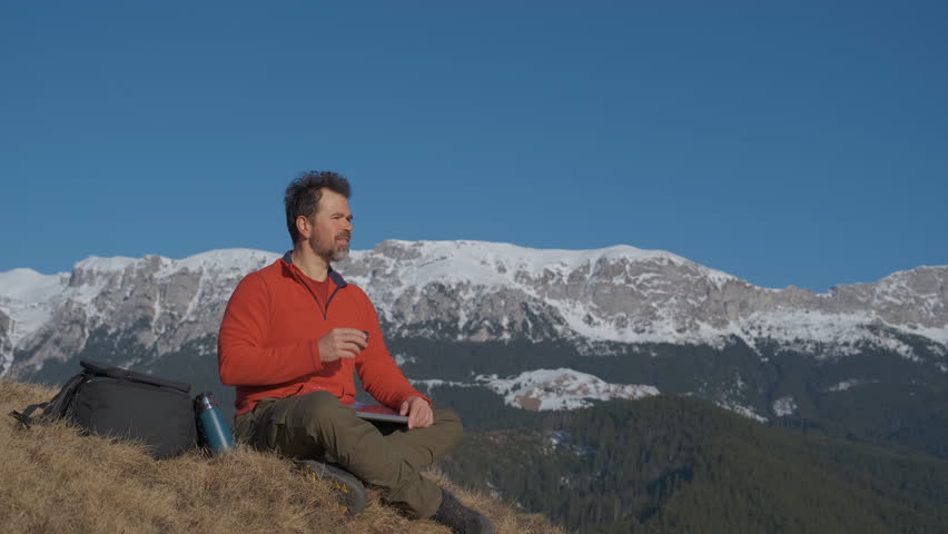 Digital nomad drinking coffee on a mountain ridge, low angle close up