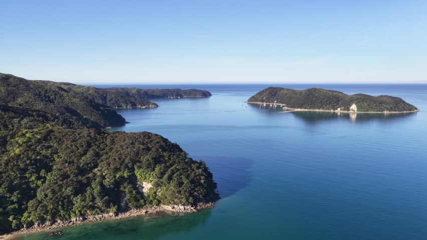 Aerial drone footage over a scenic bay with forested islands and calm blue water in New Zealand South Island with a small coastal settlement visible.