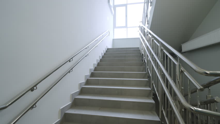 Wide staircase leads toward bright window in modern building. High quality metal handrails ensure safety and comfort for all visitors